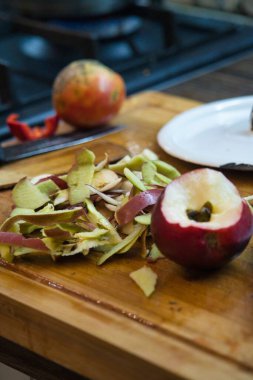 Ahşap kesim tahtası, yanında bir elma ve kesilmiş bir elma ile taze soyulmuş elma derileri sergiler. Yemek hazırlayan bir mutfağa benziyor..