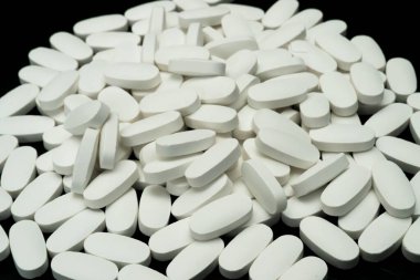 Parlak siyah bir yüzeye yayılmış sayısız beyaz oval tablet tek tip şekillerini ve renklerini göstererek çarpıcı bir görsel karşıtlık oluşturuyor..