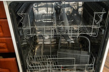 The interior of an empty dishwasher shows clean, gleaming racks, waiting to be filled with dishes after preparation and cleaning in the kitchen. clipart