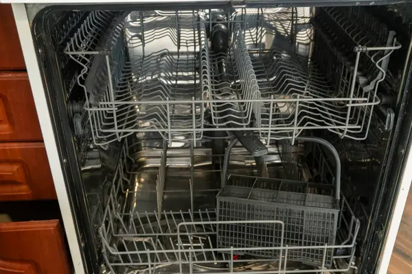 Boş bir bulaşık makinesinin içi temiz, pırıl pırıl raflar gösteriyor, hazırlandıktan sonra bulaşıklarla doldurulmayı bekliyor ve mutfağı temizliyor..