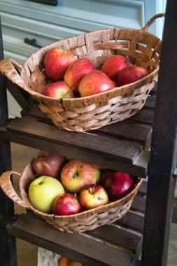 Two woven baskets filled with red and green apples rest on wooden shelves in a cozy kitchen, showcasing a vibrant and inviting arrangement of produce. clipart