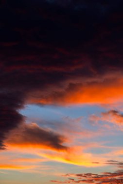 Çarpıcı bir günbatımı, gökyüzündeki kara bulutlara karşı canlı turuncu renklerin bir karışımını sergiler. Alacakaranlık sırasında dramatik ve sakin bir atmosfer yaratır..