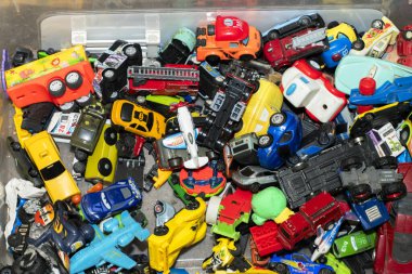 Renkli oyuncak arabalardan oluşan bir karmaşa temiz bir depo kutusunu dolduruyor, çeşitli şekil ve boyutlarda sergileniyor. Bu oyuncaklar eğlenceli ve nostaljik bir atmosfer yaratıyor..