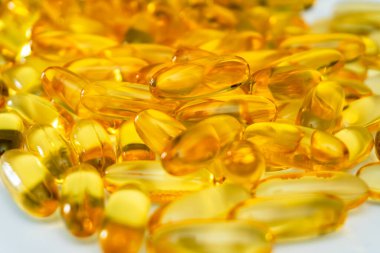 Parlak sarı jel kapsülleri bir yüzeye dağılmış, görsel olarak çekici bir düzenleme yaratıyor. Güneş ışığı, pürüzsüz yüzeylerinden yansıyarak parıltılarını arttırır..