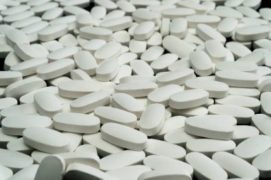 Yüzlerce beyaz oval tablet düz bir yüzeye yakın bir şekilde dağılmıştır. Düzenleme, eczane vitrinini andıran, yoğun bir görünüm yaratıyor..