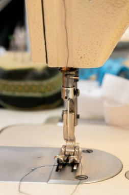 Dikiş makinesinin iğnesinin detaylı görüntüsü, ütücü ayak ve dikiş projesinin ortasındaki iplik, zanaatın karmaşık mekaniğini yakalıyor..