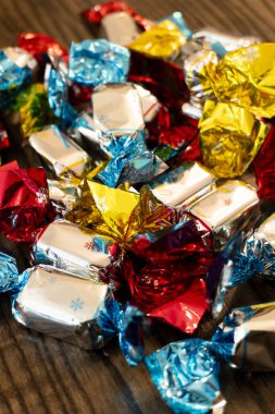 Kırmızı, mavi, sarı ve gümüşe boyanmış parlak renkli şekerler kırsal bir ahşap yüzeye saçılmış, davetkar ve şenlikli bir görüntü yaratıyor..