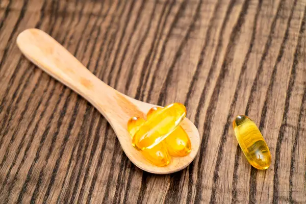 Birkaç altın jelatin kapsülü, ahşap bir kaşığa yerleştirilir. Bir kapsül, kırsal ahşap bir yüzey üzerinde uzanıp dokularını ve renklerini renklendirir..