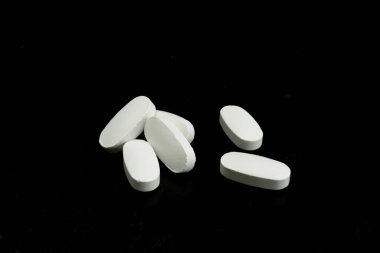 Altı beyaz tablet, oval şekillerini ve pürüzsüz dokularını vurgulayan siyah bir zemin üzerine gelişigüzel dağılmış durumda..