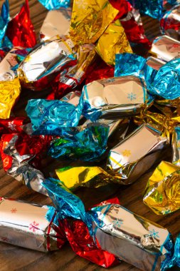 Parlak ambalajlı parlak renkli şekerler ahşap bir masaya yayılarak kırmızı, mavi ve altın folyonun bir karışımını sergiliyorlar. Dekor sıcak, davetkar bir his katıyor..
