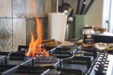 A gas stove burns with a bright flame during meal preparation. Various kitchen utensils and condiments are seen in the background, creating a vibrant atmosphere. clipart