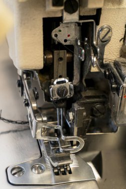 Dikiş makinesi kumaş dikmek için bir tekstil atölyesinde çalışıyor. Makinenin çeşitli parçaları görünür ve karmaşık mekanikleri gösterir.