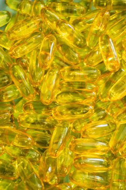 A close-up view reveals a collection of vibrant golden gelatin capsules stacked closely together, reflecting light and showcasing their translucent quality. clipart