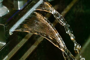 Pürüzsüz bir musluktan zarif bir şekilde akan su modern bir banyo tasarımı sergiliyor. Yansıtıcı yüzeyler akan suyun zarafetini arttırır..