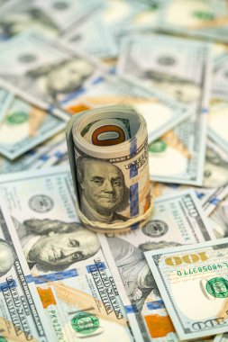 Yakın çekim, bir yüzeye yayılmış sayısız yüz dolarlık banknotlar arasında dimdik duran yuvarlanmış bir para yığınını gösteriyor..
