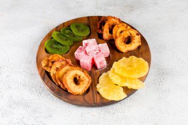 Ahşap tabakta ananas, elma ve kivinin yanı sıra renkli şekerlemeler de dahil olmak üzere çeşitli kurutulmuş meyveler sergilenerek canlı bir ikram sunuluyor..