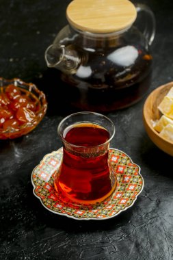 Bir bardak zengin kırmızı çay, abur cuburlarla çevrili dekoratif bir tabakta oturur. Şekerler ve jöle de dahil. Yemek saatinde davetkar bir ortam yaratır..