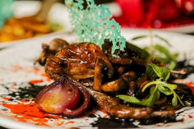 Izgara ahtapot içeren canlı bir yemek, otlar ve renkli soslarla süslenmiş, akşam yemeği sırasında bir restoranda sanatsal bir tabakta servis ediliyor..