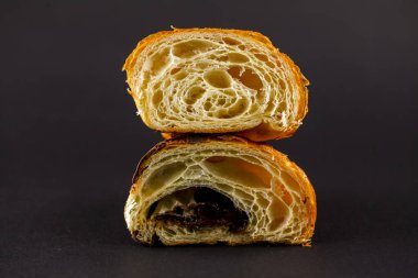 Taze pişmiş kruvasan ikiye bölünür. İçi yumuşak, pul pul dökülür ve içi çikolata doludur. Karanlık arka plan çekiciliğini arttırır.