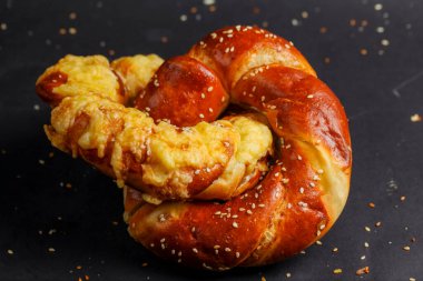 Erimiş peynire sarılı sıcak, yumuşak bir çubuk kraker koyu, dokulu bir arka planda oturur, altın-kahverengi rengini ve susam tohumlarını sergiler..