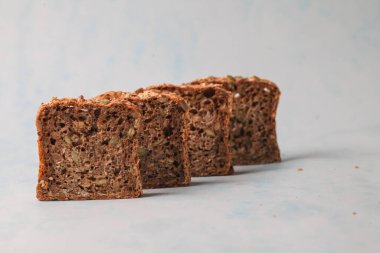 Tam tahıllı ekmek dilimleri düzgünce düzenlenir, dokuları ve malzemeleri sergilenir. Hafif arkaplan ekmeğin detaylarını vurgular.