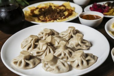 Lezzetli hamur köfteleri, canlı bir yemek toplantısında çeşitli yemek ve baharatlarla çevrili beyaz bir tabakta sunulur. Atmosfer canlı ve iştah açıcı..