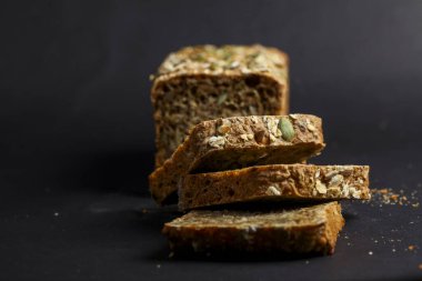Tam tahıllı ekmek dilimleri düzgünce düzenlenir. Tohumları ve yulafları olan kırsal bir doku sergilenir. Koyu arka plan ekmeğin davetkar görünümünü arttırır..