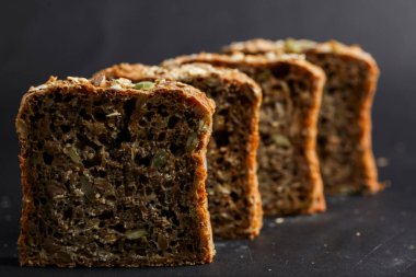 Dört dilim tam tahıllı ekmek, koyu bir arkaplana karşı sıralanmış, kabuklu dış ve sağlıklı dokularını gözler önüne seriyor..