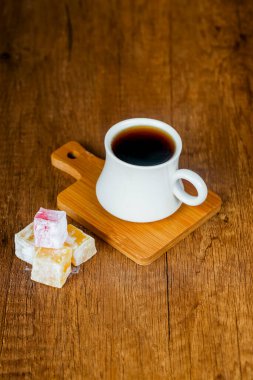 Beyaz bir kahve fincanı içinde zengin bir bira olan tahta bir tahtanın üzerinde duruyor. Yanı sıra, renkli tatlılar ayara biraz tatlılık katar.