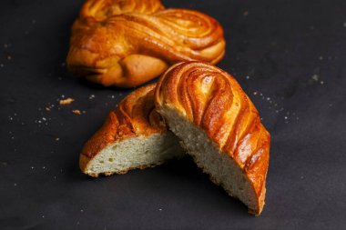 İki güzel işlenmiş ekmek rulosu karanlık bir yüzeyde oturur, biri yumuşak ve havadar dokuyu ortaya çıkarmak için kısmen dilimlenmiş. Karmaşık tasarım yeteneklerini sergiliyorlar..