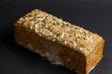 Taze pişmiş tohum ve kabak tohumlarıyla kaplı fındık ekmeği koyu bir yüzeye oturmuş, dokusunu ve sağlıklı beslenmek için mükemmel malzemelerini vurguluyor..