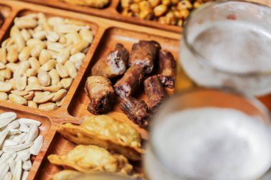 Ahşap bir tabakta iki bardak biranın yanında fındık, kurutulmuş et ve hamur işleri de dahil olmak üzere çeşitli atıştırmalıklar sergilenir..