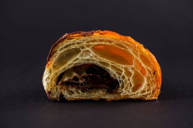 Yumuşak bir pastanın enine kesitinde zengin çikolata dolgusu ve katmanlı yapısı karanlık bir arka plana karşı sergilenir ve cazip görünümünü vurgular..