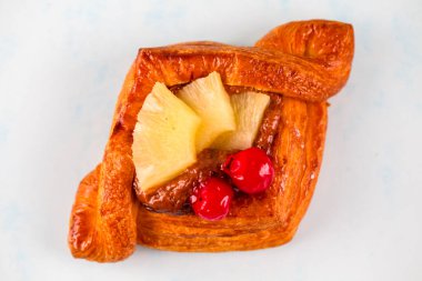 A delicious pastry showcases a golden-brown crust topped with sweet pineapple and bright red cherries, inviting viewers to savor its delightful flavor. clipart