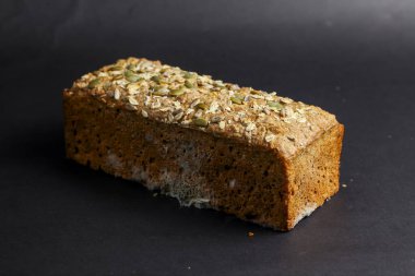 Üstünde çıtır çıtır tohum olan taze pişmiş bir ekmek karanlık bir yüzeyde duruyor. Altın kabuk ve yumuşak iç kısımlar her yemek için mükemmel, sıcak bir ısırık ister..