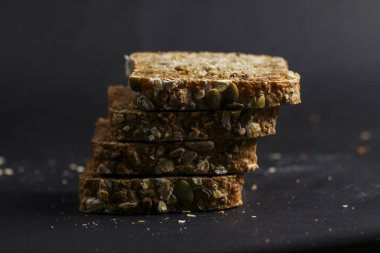 Dört dilim tam tahıllı ekmek, yoğun dokularını ve karışık tahıl bileşenlerini yumuşak ışıklandırma altında sergiliyor..