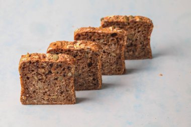 Dört dilim tam tahıllı ekmek pürüzsüz mavi bir zemin üzerinde sıralanmış görünür tohumlar ve taneciklerle dokulu bir kabuk sergiliyor..