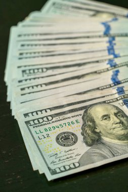 Yüz dolarlık banknotlar düzgünce dizilmiş, karanlık bir masanın üzerindeki karmaşık tasarımları ve güvenlik özelliklerini sergiliyorlar..