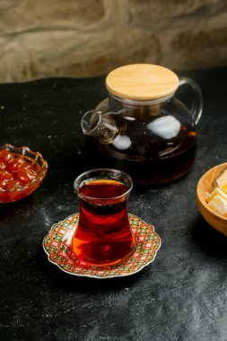 Bir bardak aromatik çay güzel desenli bir tabağa yerleştirilir, bir çaydanlık ve geleneksel şekerlerle çevrili, sıcak ve davetkar bir atmosfer yaratır..