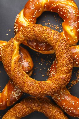 Çeşitli taze pişmiş susamlı simitler sanatsal bir şekilde koyu bir yüzeyde sergilenir. Altın renklerini ve davetkar görünüşlerini sergilerler..