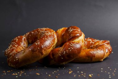 Işıl ışıl yüzeyi ve serpiştirilmiş susam tohumlarıyla üç taze pişmiş kraker koyu bir zemin üzerinde oturur ve altın-kahverengi rengini ve dokusunu sergilerler..