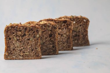 Yoğun, zanaatkar ekmek dilimleri açık mavi arkaplana karşı sırayla dizilir ve her dilimdeki zengin dokuyu ve çeşitli tohumları gösterir..