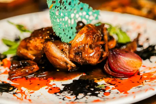 Güzel hazırlanmış bir bıldırcın tabağı renkli soslar, süslemeler ve kızarmış sebzelerle sunulur. Lüks bir yemek deneyimi için mükemmeldir..