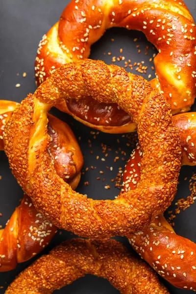 Çeşitli taze pişmiş susamlı simitler sanatsal bir şekilde koyu bir yüzeyde sergilenir. Altın renklerini ve davetkar görünüşlerini sergilerler..