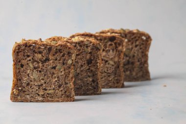 Dört dilim tam tahıllı ekmek soluk bir yüzeyde düzgün bir şekilde sıralanır, yoğun dokularını ve tohumlarını sergiler, sağlıklı malzemeleri ve sağlıklı beslenmeyi vurgularlar..