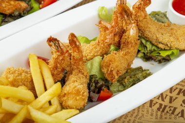 Crispy fried shrimp are beautifully arranged on a white platter alongside golden fries, fresh lettuce, and vibrant tomatoes, creating an appetizing dish.