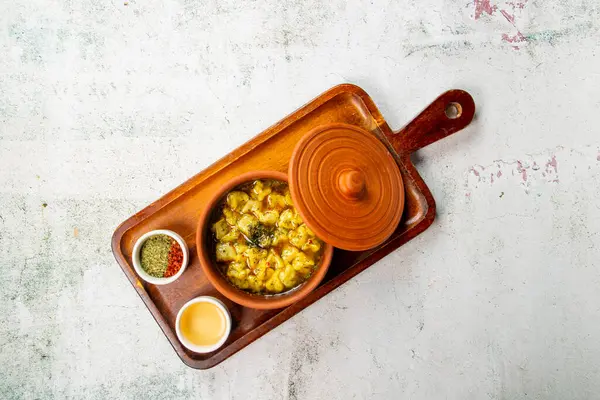 İçinde sebze ve baharat karışımı bulunan kilden bir tencerede sunulan canlı bir yemek. Eşlik eden sos ve baharatlar lezzetli bir yemek deneyimi için ilave lezzet sunar.