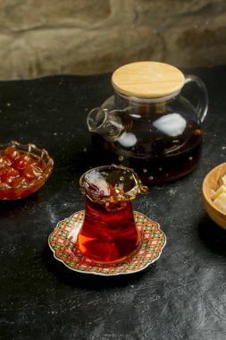 Parlak kırmızı Türk çayı, çeşitli tatlılar ve çaydanlıkla birlikte zarif bir şekilde dekoratif bir bardağa dökülüyor. Yerleşim sıcaklığı ve konukseverliği yayar..
