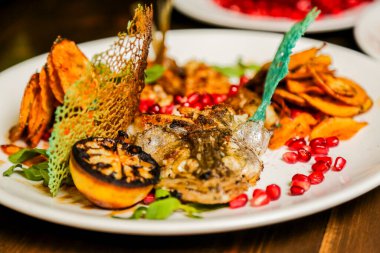 Çok güzel sunulmuş gurme yemek vitrinleri ızgara balık, nar tohumu, patates cipsi ve beyaz tabakta servis edilen canlı yeşil ve mavi garnitürler..