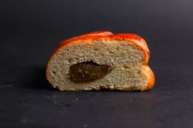 Yarım parça yuvarlak ekmek, içindeki yumuşak tatlı dolguyu ortaya çıkarır. Kabuk, zıt bir karanlık yüzeye karşı altın renginde parlar..